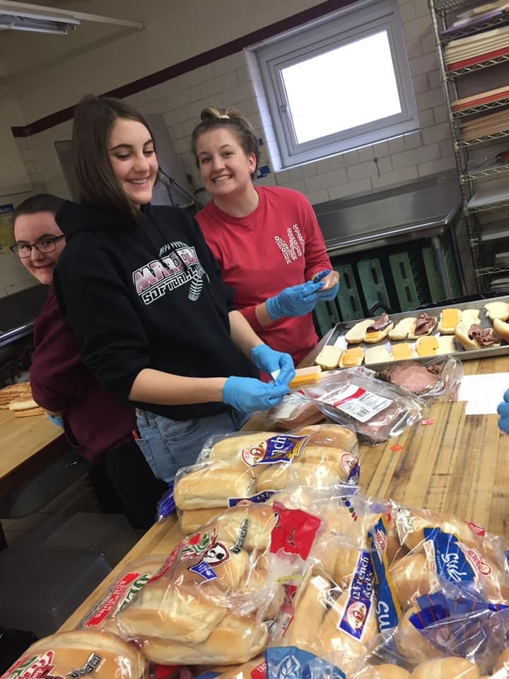 Two students smiling and making sandwiches.
